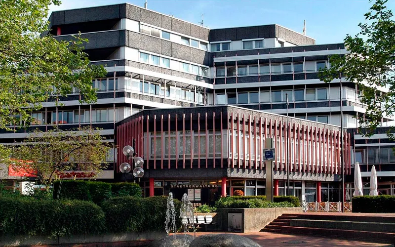 Stadtverwaltung mit moderner Architektur, umgeben von Grünflächen und Bäumen. Blick auf die Fassade und vordere Eingangsbereich.