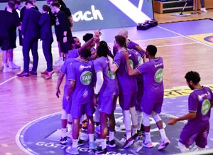 Mehrere Basketballspieler in lila Trikots umarmen sich auf dem Spielfeld nach einem Spiel.