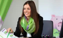 Lächelnde Frau mit einem grünen Schal, die an einem Tisch sitzt und auf ein Dokument zeigt.