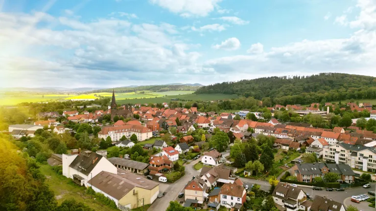 Luftbild eines kleinen Dorfes, umgeben von Bäumen, Wäldern und Hügeln.