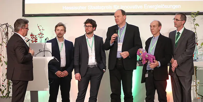 Gruppenszene bei der Verleihung des Hessischen Staatspreises für innovative Energielösungen, Personen mit Mikrofon und Preis.