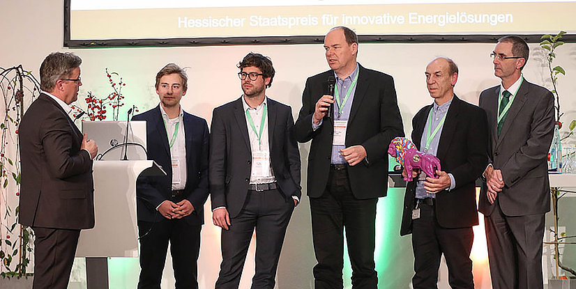 Gruppenszene bei der Verleihung des Hessischen Staatspreises für innovative Energielösungen, Personen mit Mikrofon und Preis.
