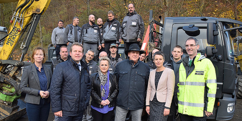 Gruppenfoto von Mitarbeitern und Vertretern bei einem Arbeitsgerät, umgeben von Baustellenumgebung und Maschinen.
