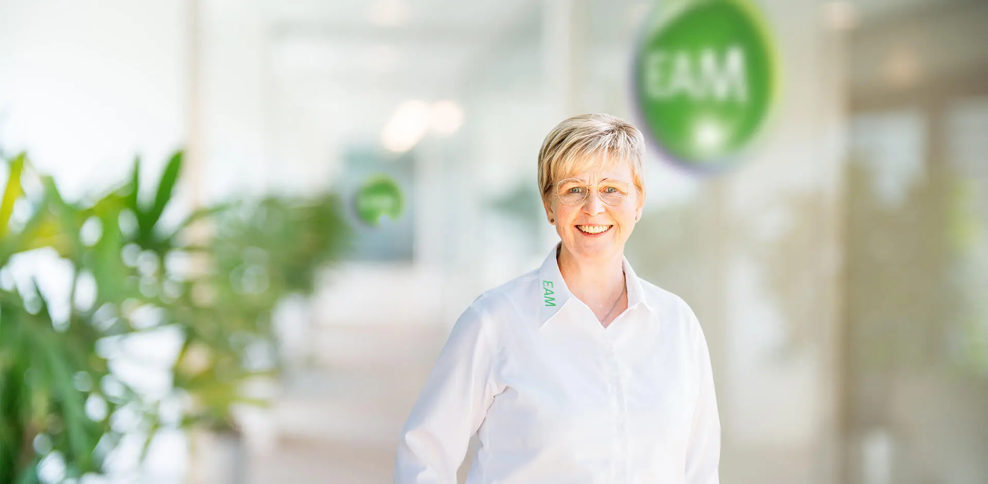 Eine Frau mit kurzen Haaren lächelt, im Hintergrund das EAM Logo
