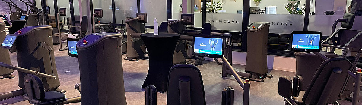 Alt-Tag: Moderne Fitnessgeräte in einem stilvollen Gym mit Bildschirmen und einem runden Tisch.