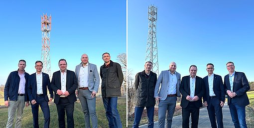 Zwei nebeneinander angeordnete Fotos zeigen jeweils eine Gruppe von sechs Personen, die im Freien vor einem hohen Funkmast stehen. Der Himmel ist klar und blau. Die Personen stehen in einer Reihe, tragen überwiegend formelle oder halbformelle Kleidung wie Anzüge, Hemden und Jacken. Hinter ihnen befinden sich Wiesenflächen, Wege und Bäume. Der Funkmast ragt jeweils deutlich in den Himmel und bildet den zentralen Hintergrund der Szenen.