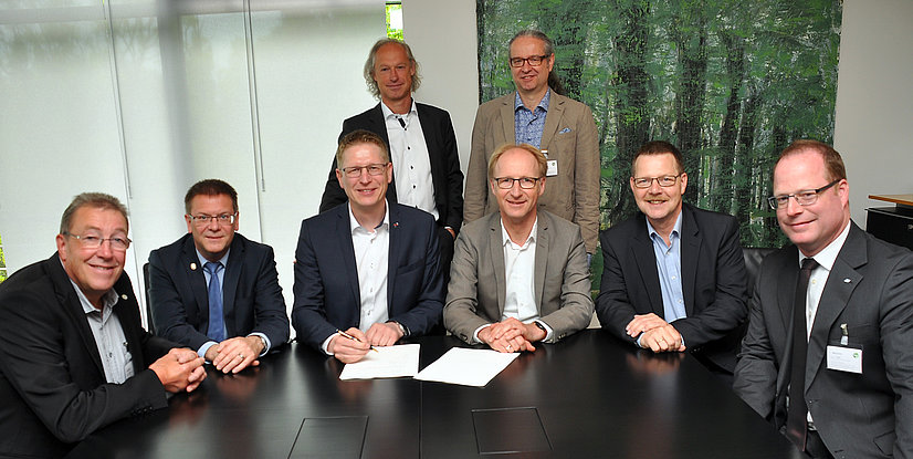 Gruppensitzung mit acht Personen am Tisch, welche Dokumente signieren.