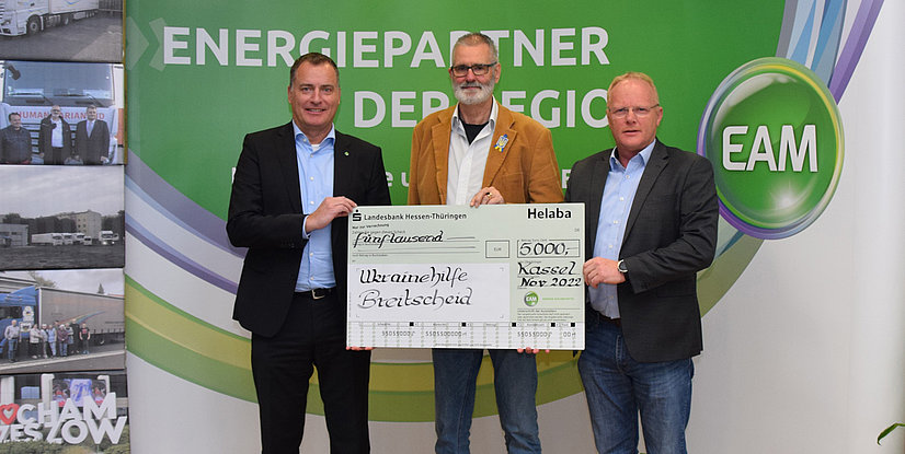 Drei Männer halten einen großen Scheck über 5000 Euro für Ukrainehilfe Breitscheid, vor einem grünen Hintergrund.
