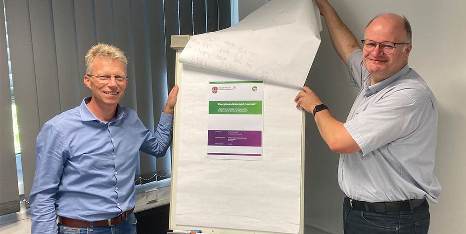 Zwei Personen lächeln, während sie ein Plakat mit dem Titel "Energiewendekonzept Neusalz"" enthüllen."