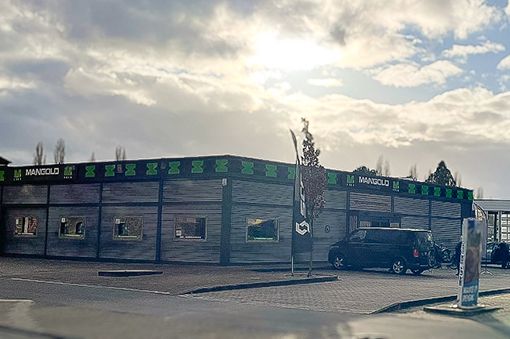Moderne Fassade eines Gebäudes mit dem Schriftzug "MANGOLD"" und einem Fahrzeug auf dem Parkplatz."