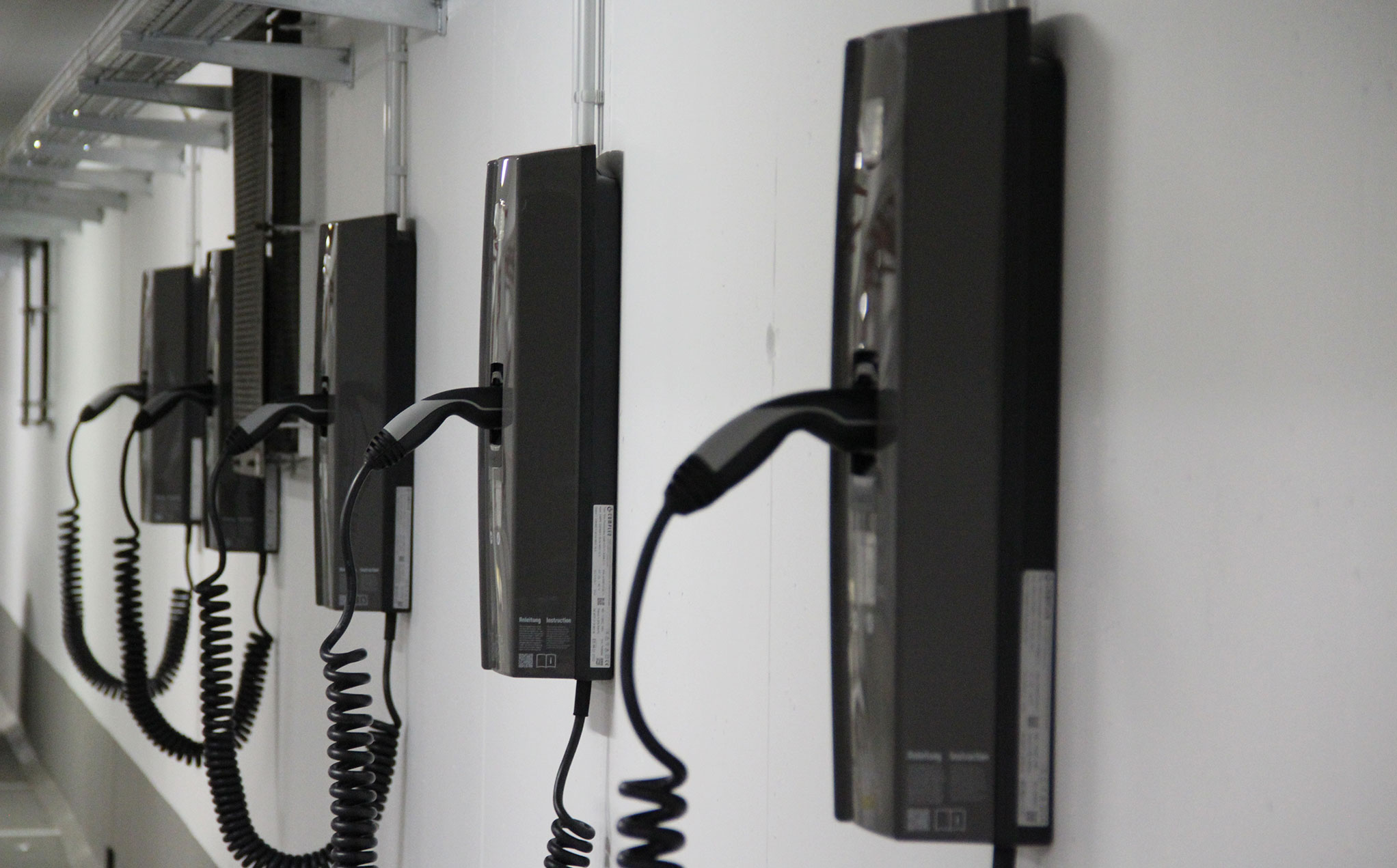 Mehrere schwarze E-Ladesäulen hängen an einer weißen Wand.
