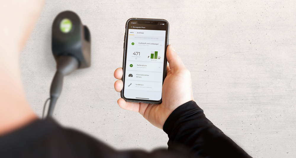 Hand hält ein Smartphone mit einer App zur Anzeige von Fahrzeugdaten vor einem grauen Hintergrund.