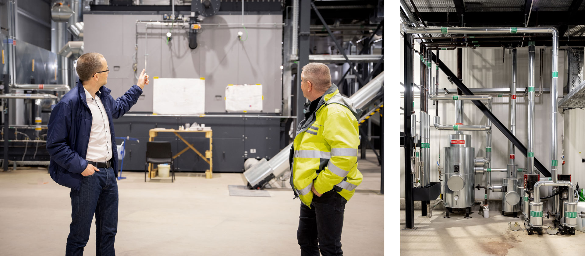 Zwei Männer im Industrieumfeld, einer zeigt auf eine Wand mit Zeichnungen, der andere blickt aufmerksam. Rohrleitungen im Hintergrund.