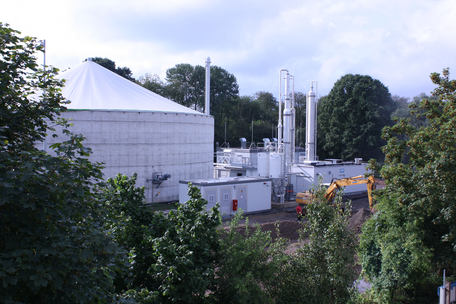 Industrieanlage mit Biogasanlage, umliegendem Grün und Bauarbeiten im Vordergrund.