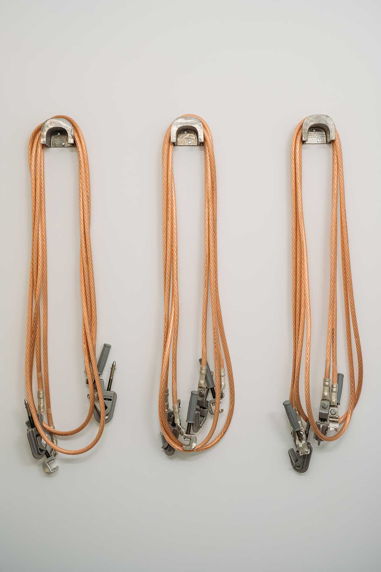 Drei orangefarbene Kletterseile mit Metallbeschlägen hängen an einer Wand.