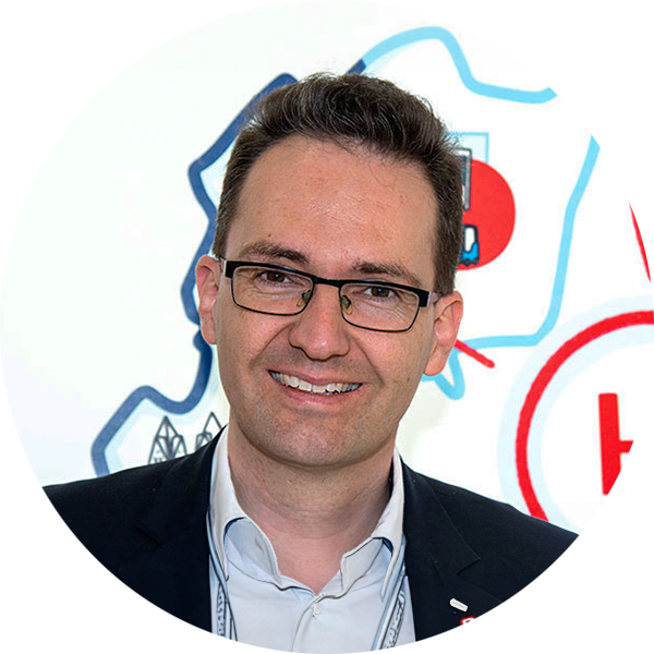 Lächelnder Mann mit Brille vor einem farbigen Hintergrund, lässig gekleidet, im Kreisformat.