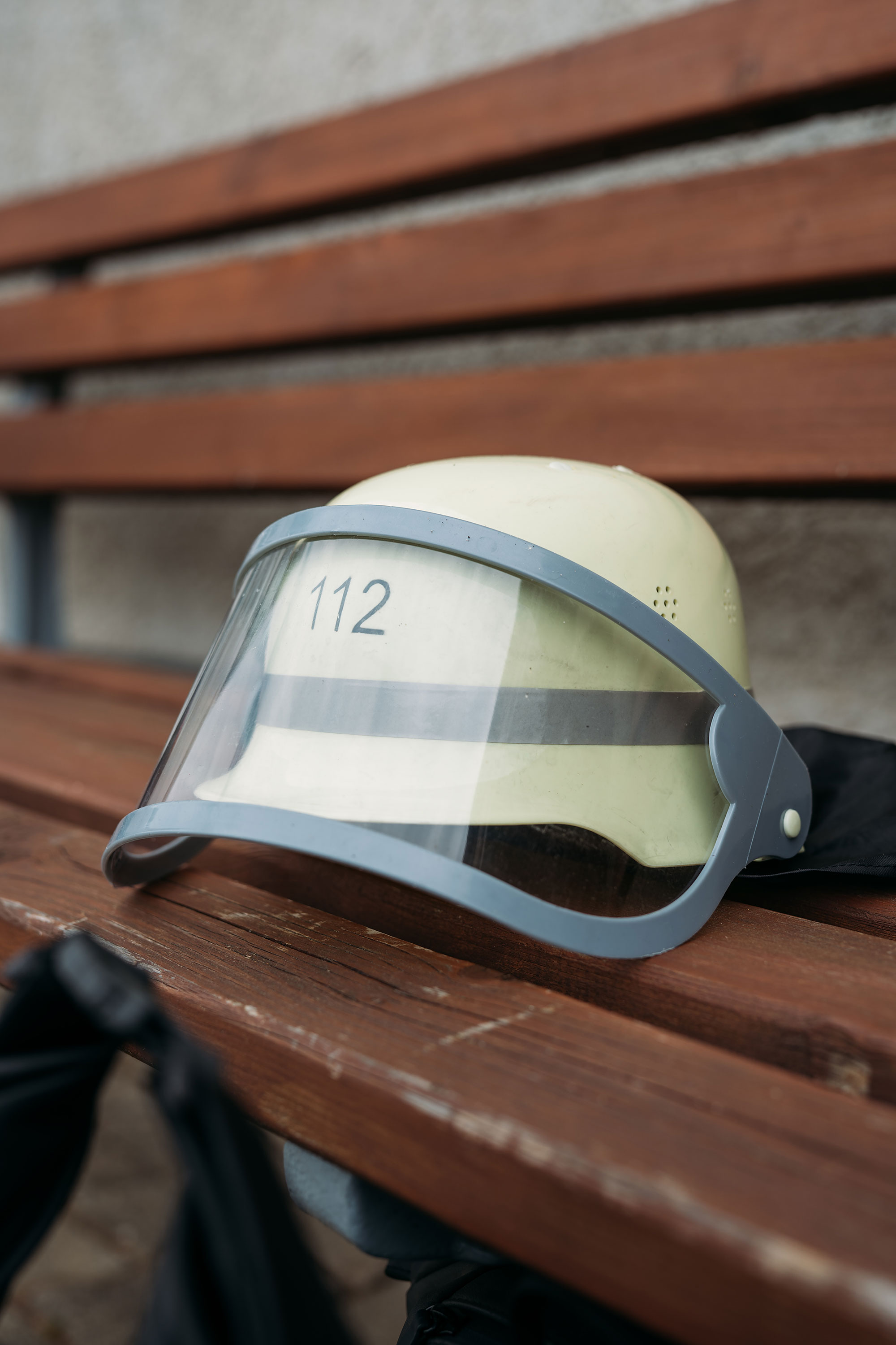 Ein gelber Feuerwehrhelm mit Sichtschutz und der Nummer 112 liegt auf einer Holzbank.