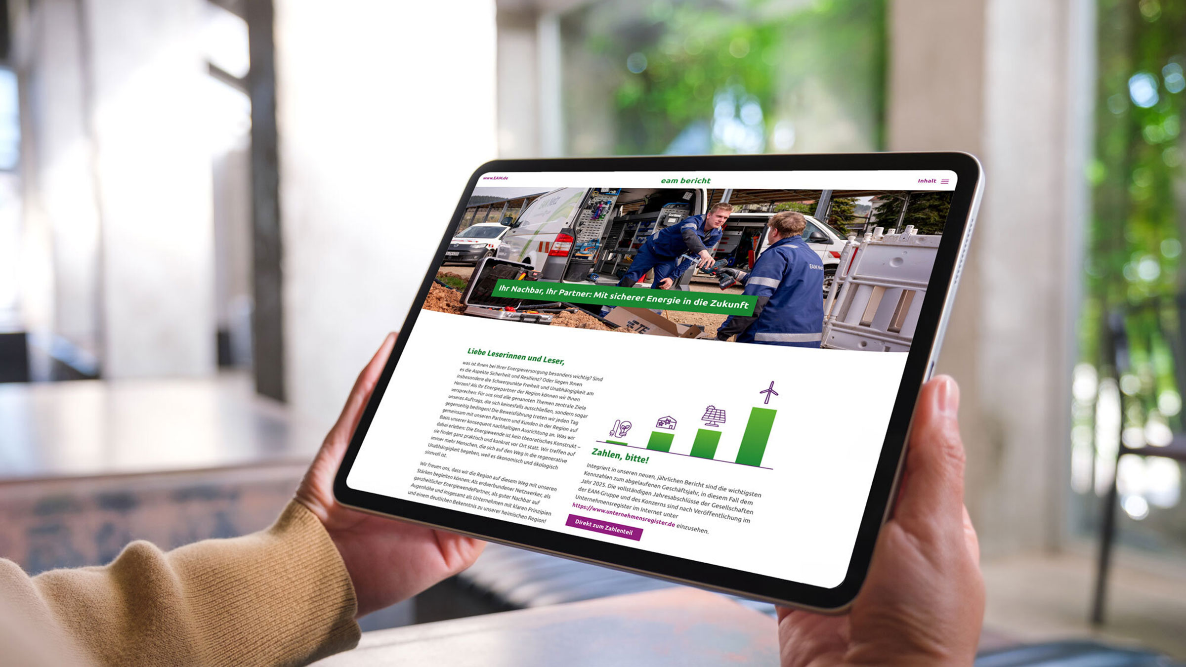 Eine Person hält ein Tablet in den Händen. Auf dem Bildschirm ist die digitale Version eines EAM-Berichts zu sehen, mit einem großen Titelbild von Mitarbeitenden bei Arbeiten an einem Servicefahrzeug sowie Text- und Grafikbereichen zum Thema sichere Energieversorgung.