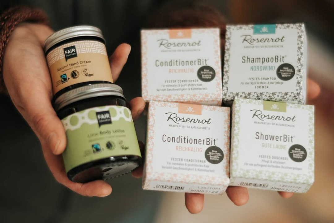 Person hält fünf Naturkosmetik-Produkte: zwei Cremes und drei feste Shampoos oder Conditioner in dekorativen Verpackungen.