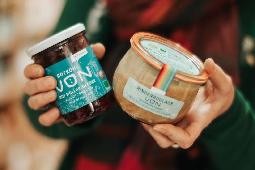 Zwei Gläser in Händen: Rotkohl und Rinderroulade, beide mit etikettierten Produkten.