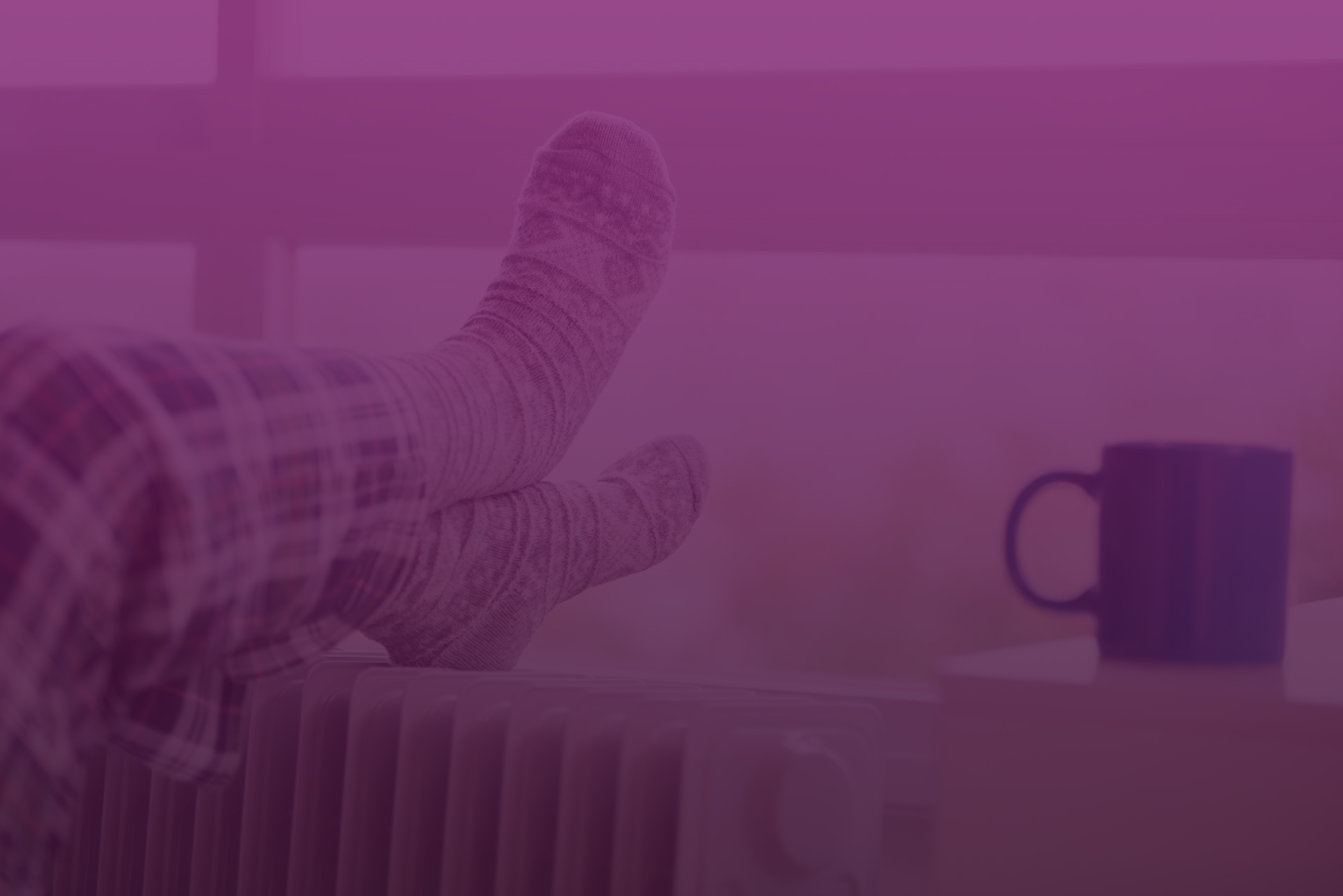Füße in Socken relaxen auf einer Heizung, neben einer Tasse Kaffee auf einem Tisch.