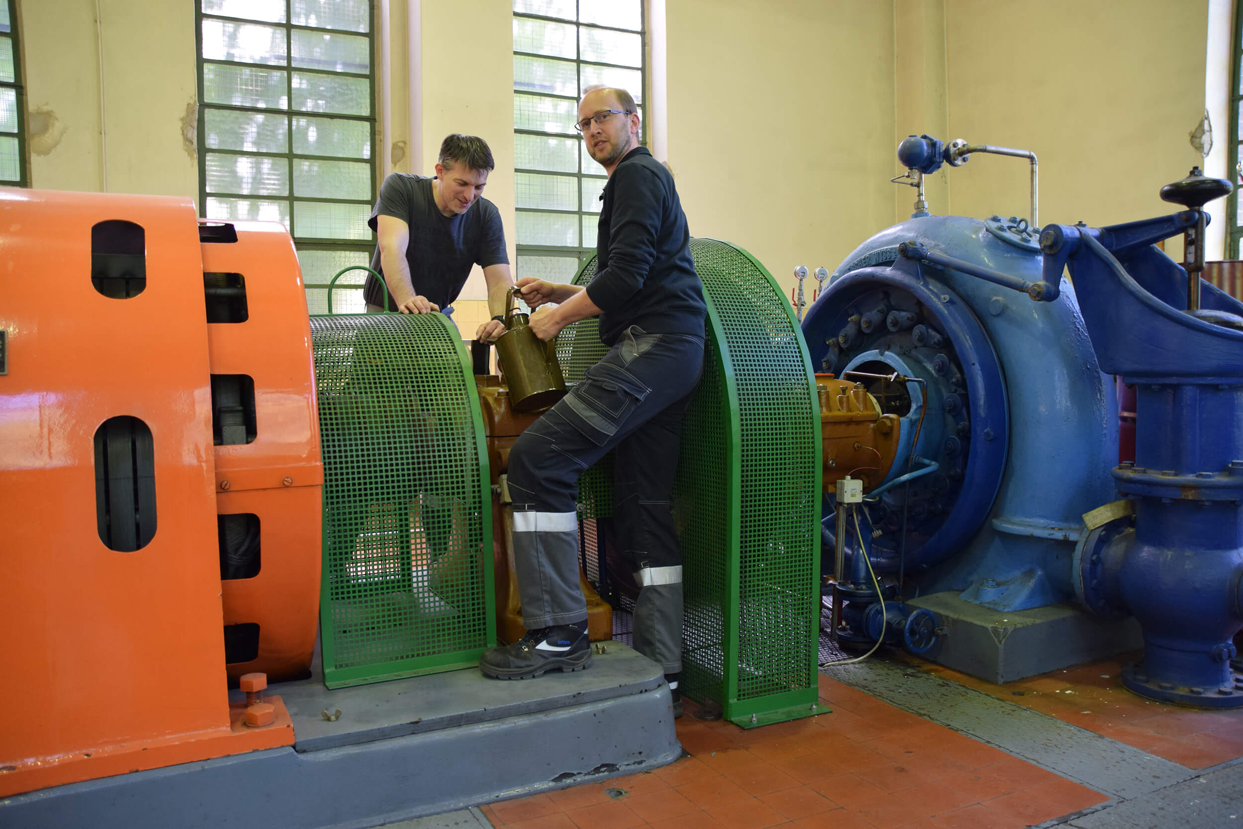 Zwei Techniker arbeiten an einer großen Maschine in einer Industriehalle, um Wartungsarbeiten durchzuführen.
