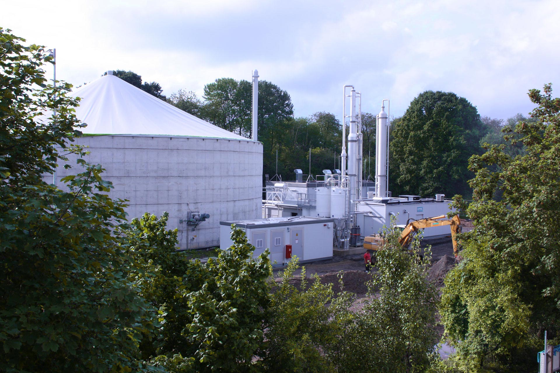 Auf dem Bild sind ein Biogasanlage und umliegende Bäume sowie Erdbewegungsarbeiten zu sehen.