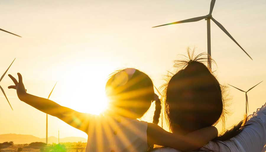 Kind und Erwachsene blicken bei Sonnenuntergang auf Windräder.