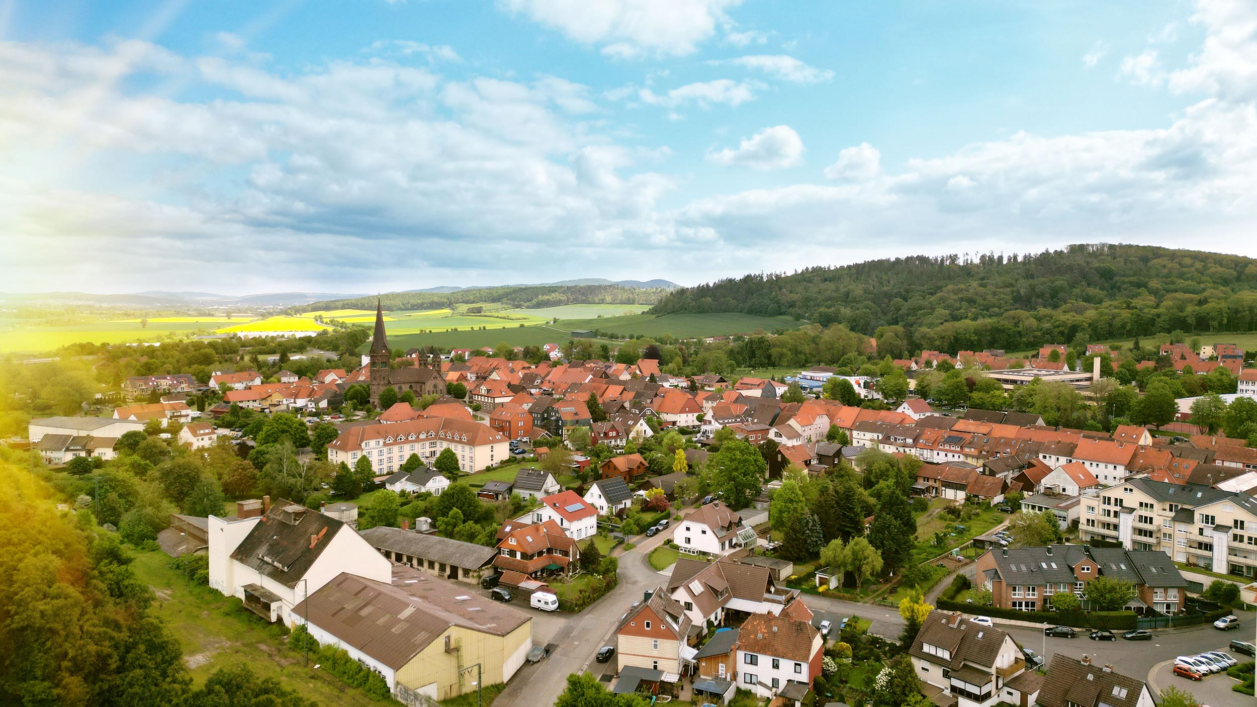 Luftbild eines kleinen Dorfes, umgeben von Bäumen, Wäldern und Hügeln.