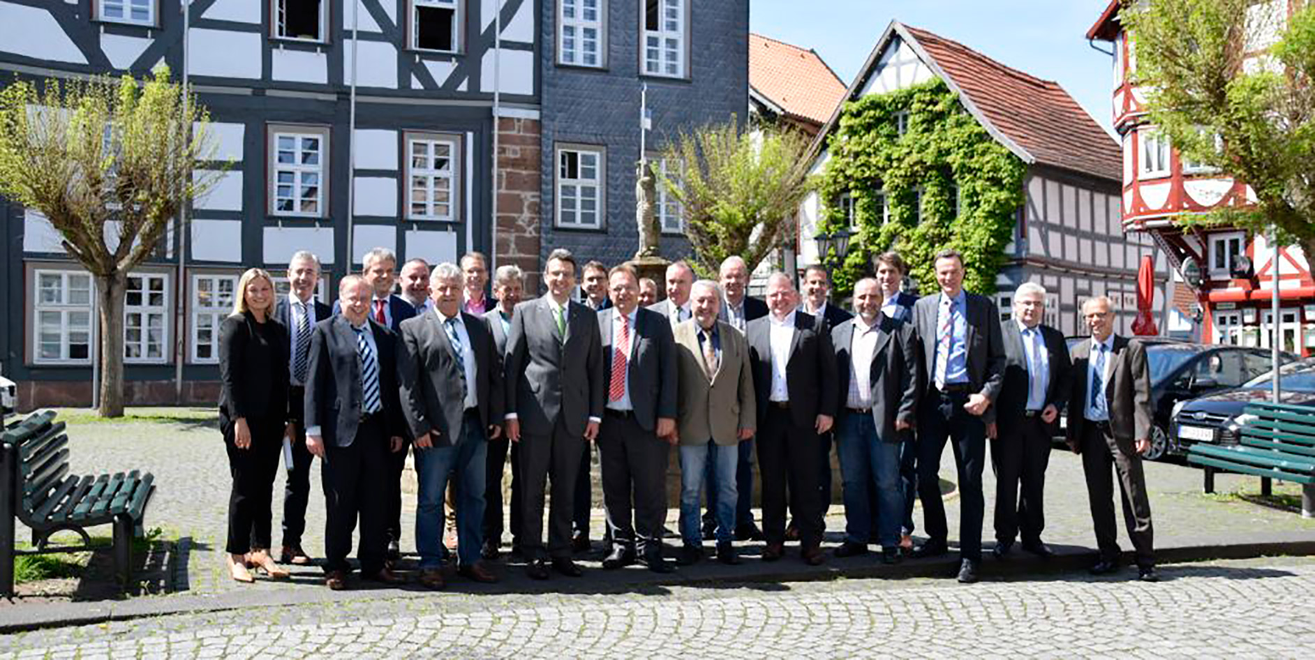 Gruppenfoto von Personen in einer Stadt mit historischen Gebäuden im Hintergrund, unter blauem Himmel.
