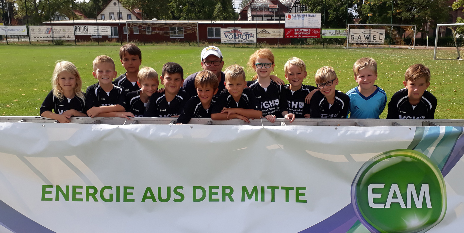 Junge Fußballmannschaft posiert lächelnd hinter einem Banner mit der Aufschrift Energie aus der Mitte
