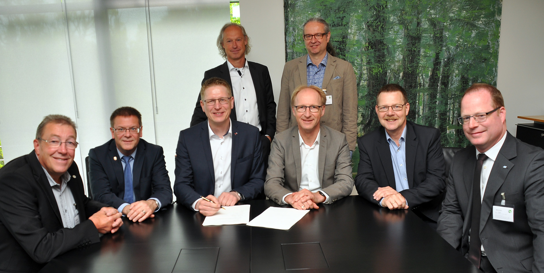 Gruppensitzung mit acht Personen am Tisch, welche Dokumente signieren.