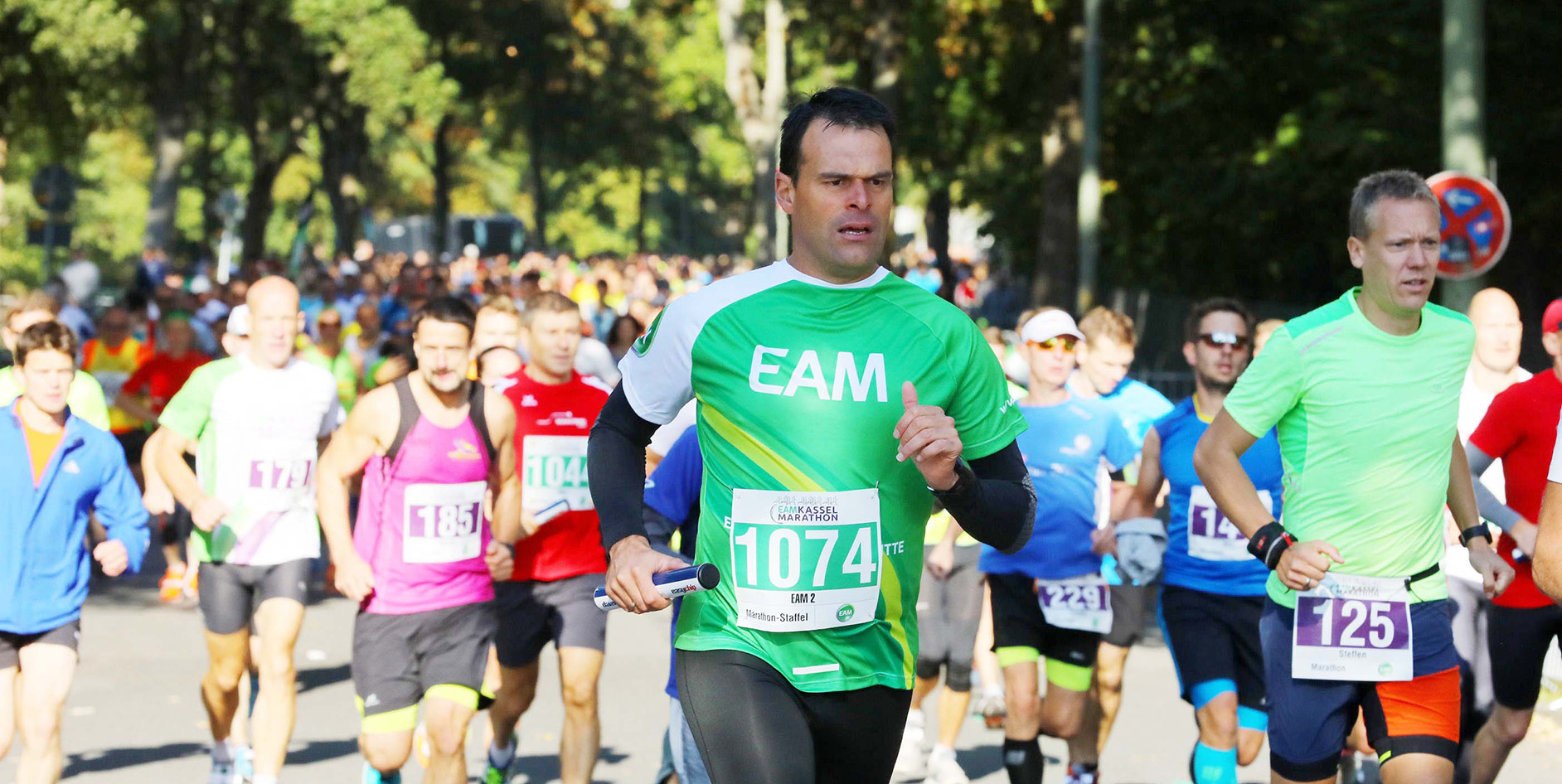 Läufer in bunten Trikots nehmen an einem Marathon teil, zahlreiche Teilnehmer sind im Hintergrund sichtbar.