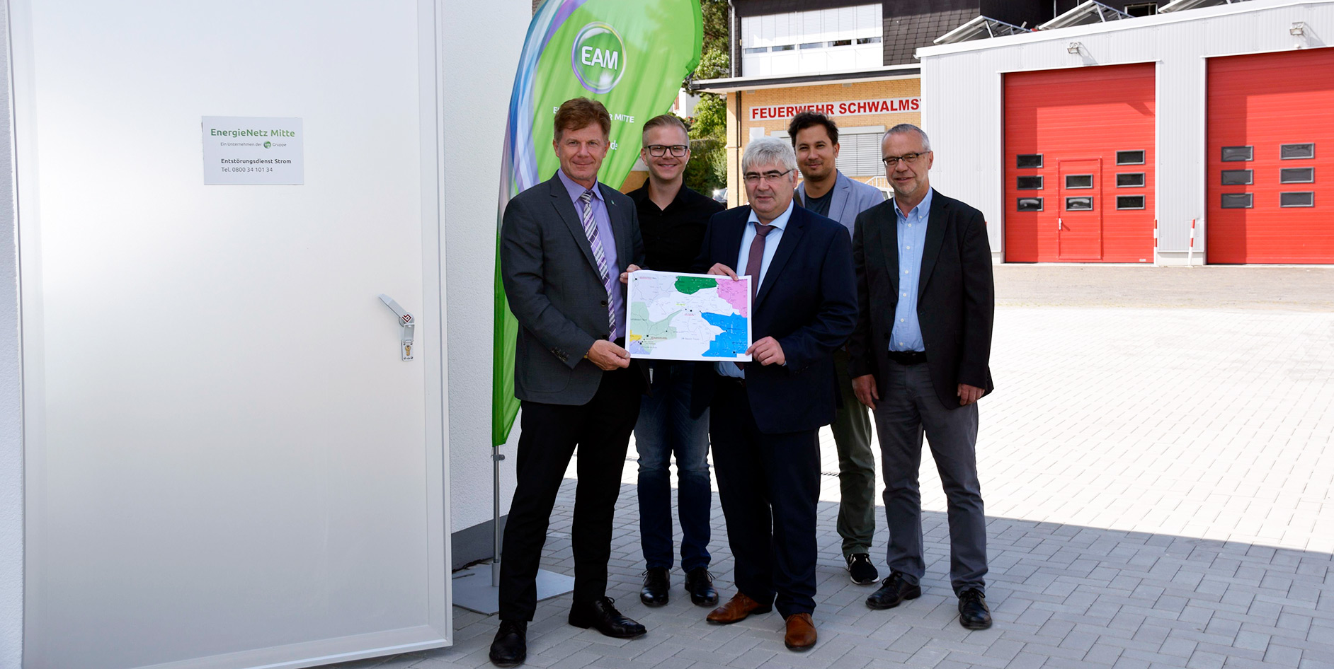 Fünf Personen präsentieren eine Karte vor einem Gebäude, gekennzeichnet mit EnergieNetz Mitte