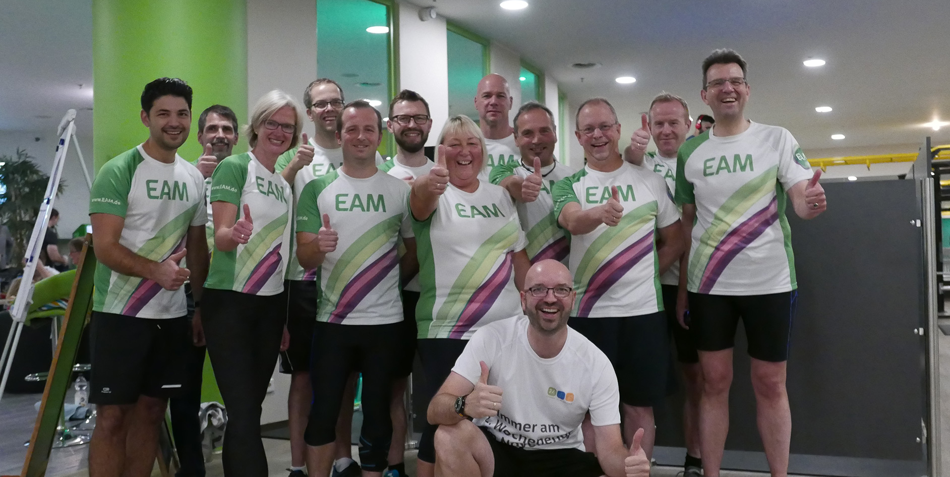 Gruppe von Personen in sportlichen T-Shirts, die Daumen hoch zeigen, in einem Fitnessstudio.