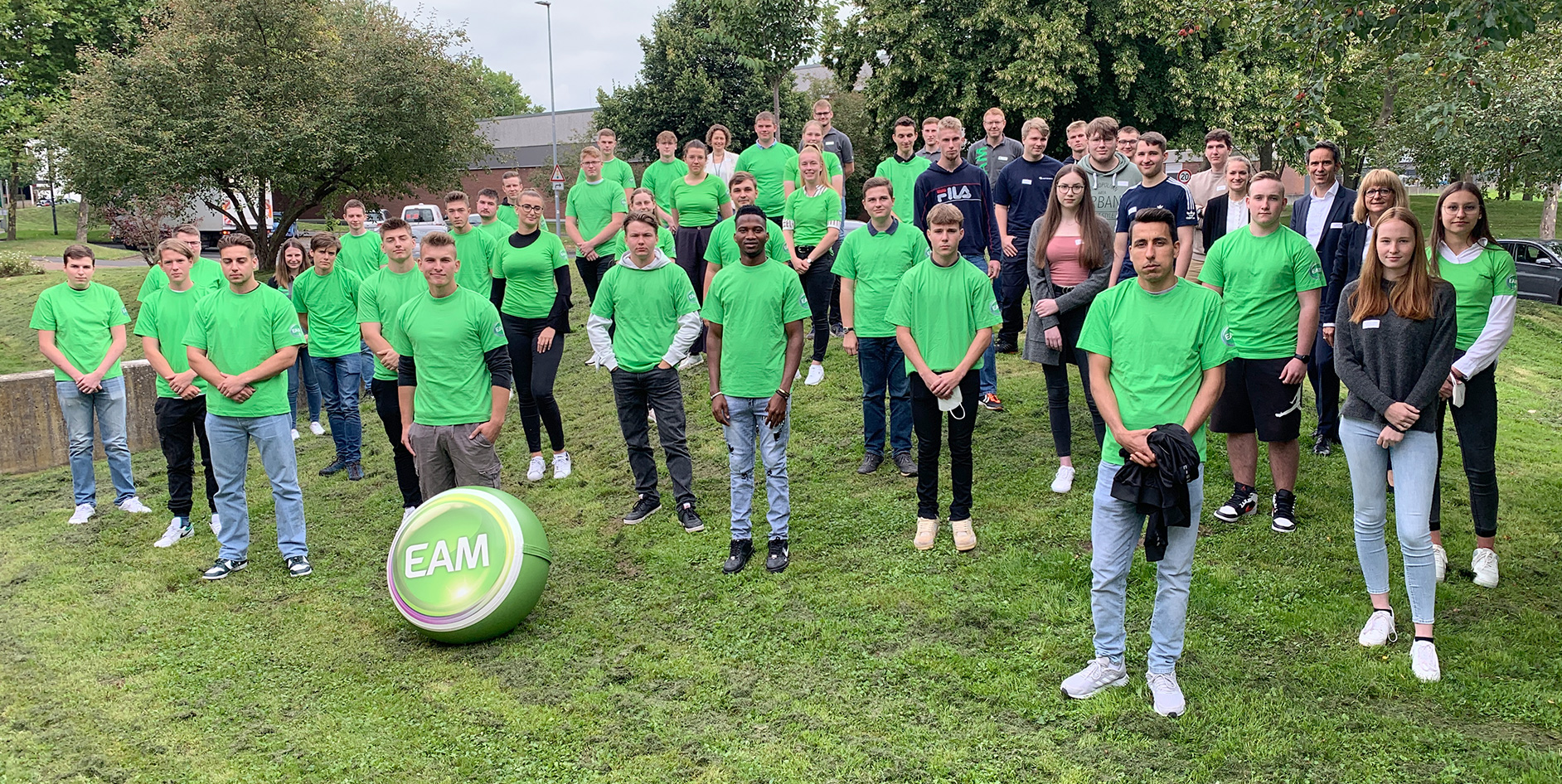 Gruppenbild der neuen Auszubildenden in grünen T-Shirts vor einem Baum, mit einem großen grünen Ball mit EAM-Logo im Vordergrund.