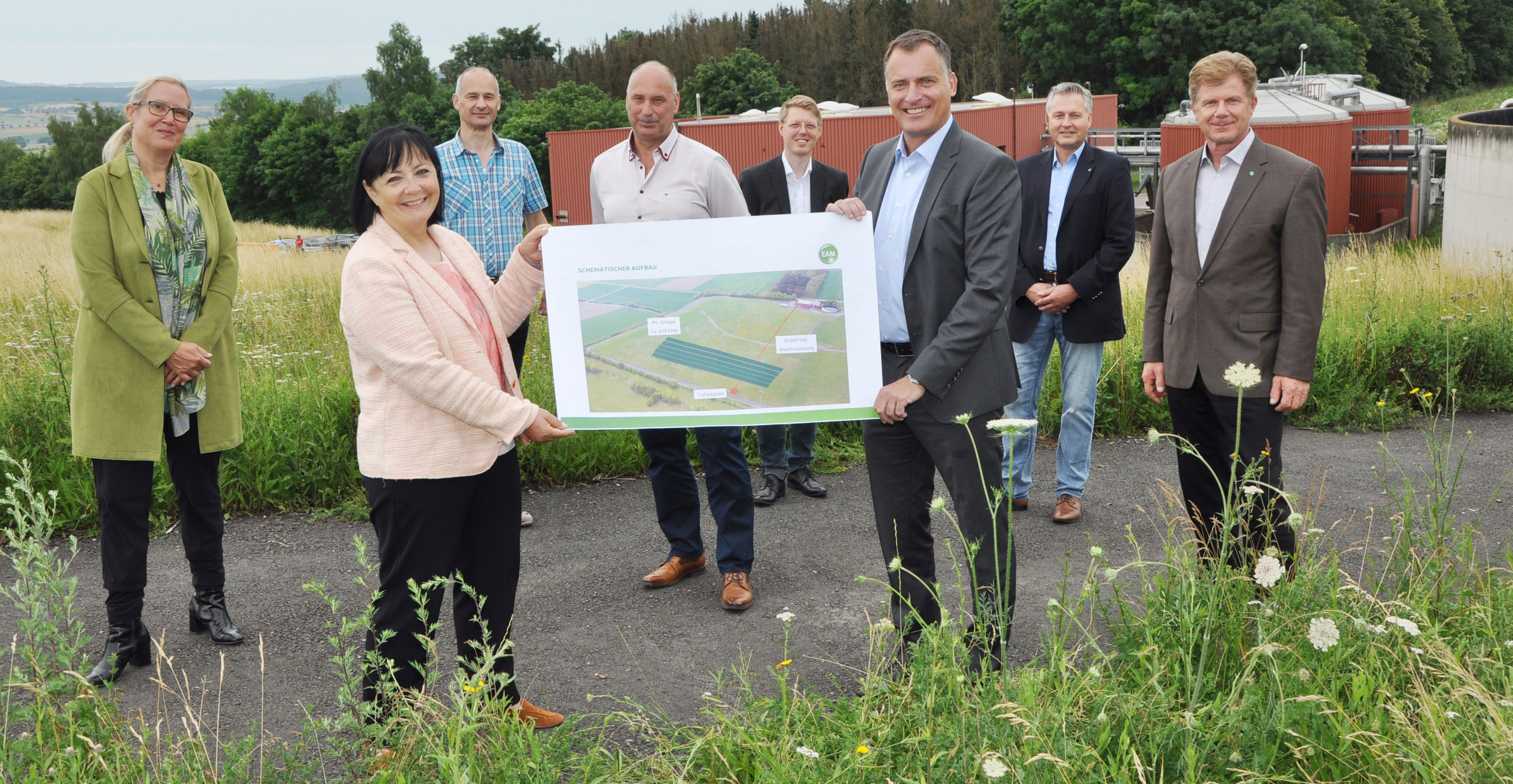 Gruppenfoto im Freien zur Vorstellung eines Plans für eine landwirtschaftliche Fläche mit Farbschema und Beschriftungen.