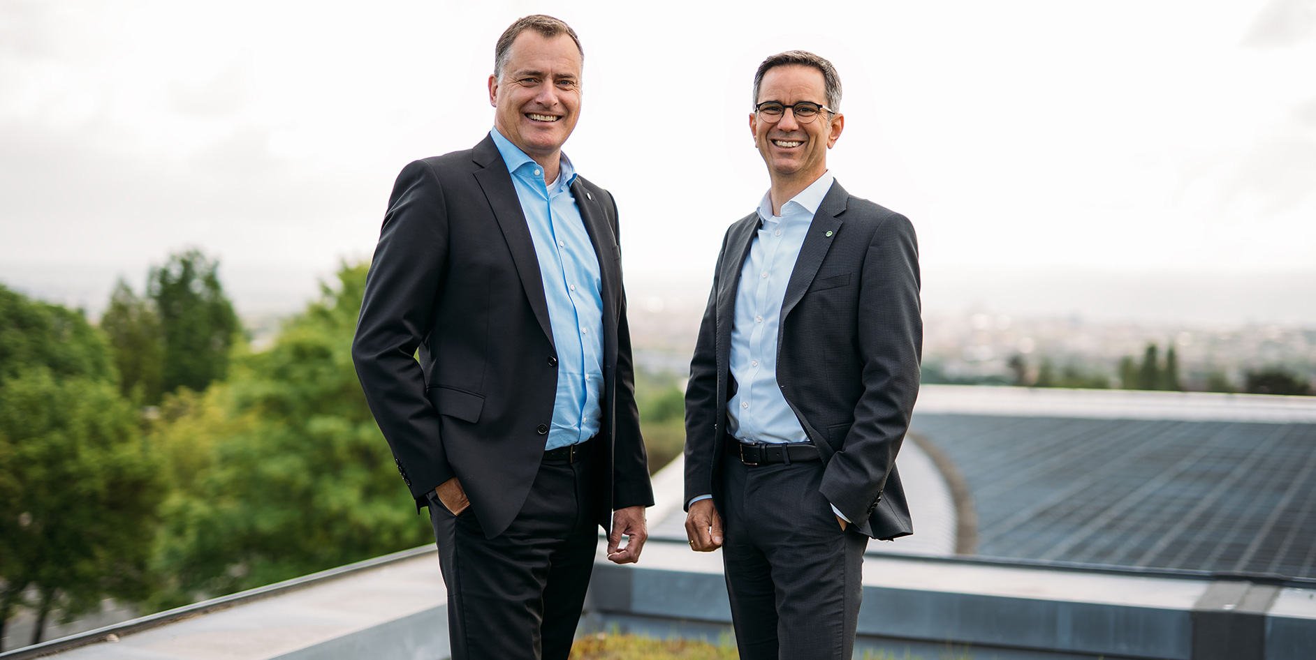 Die EAM-Geschäftsführer Olaf Kieser und Hans-Hinrich Schriever stehen auf dem Dach eines Gebäudes, im Hintergrund Solarmodule und grüne Bäume..