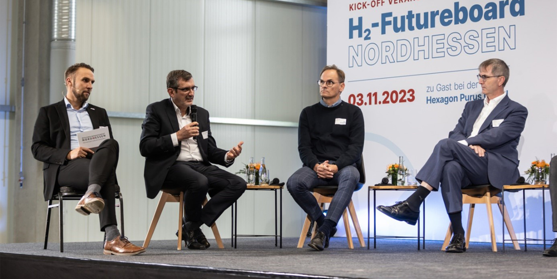 Diskussionsteilnehmer auf einer Bühne während der Veranstaltung H2-Futureboard Nordhessen, mit Stühlen und Tischen, moderner Raum.