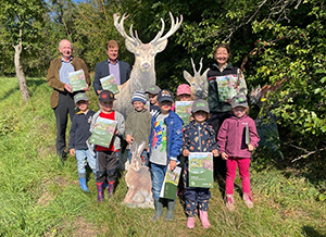 Gruppe von Kindern und Erwachsenen in der Natur, posierend mit Broschüren, vor einem Hirsch-Standbild.