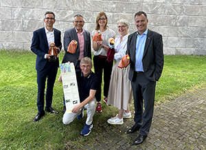 Sechs Personen stehen auf einer grünen Wiese, halten kleine Geschenke und posieren für ein Foto.