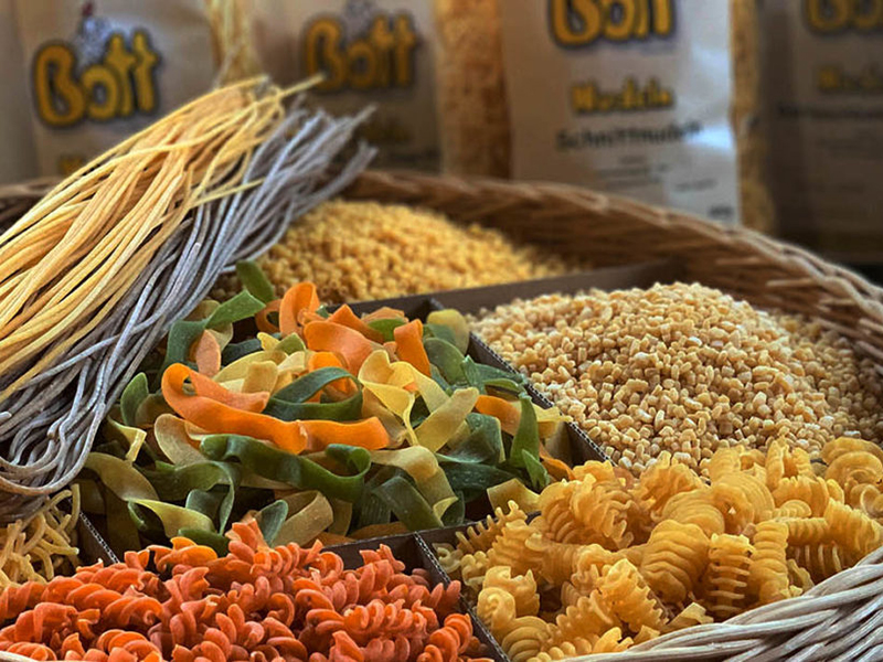 Bunte Auswahl an verschiedenen Pasta-Sorten in einem Korb, umgeben von anderen Teigwaren.