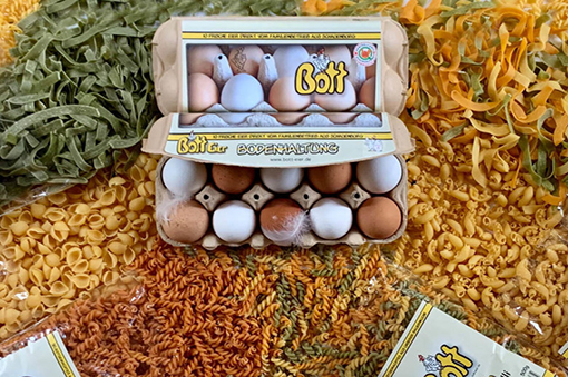 Verpackung mit Eiern in einem Körbchen, umgeben von bunten Pastasorten.