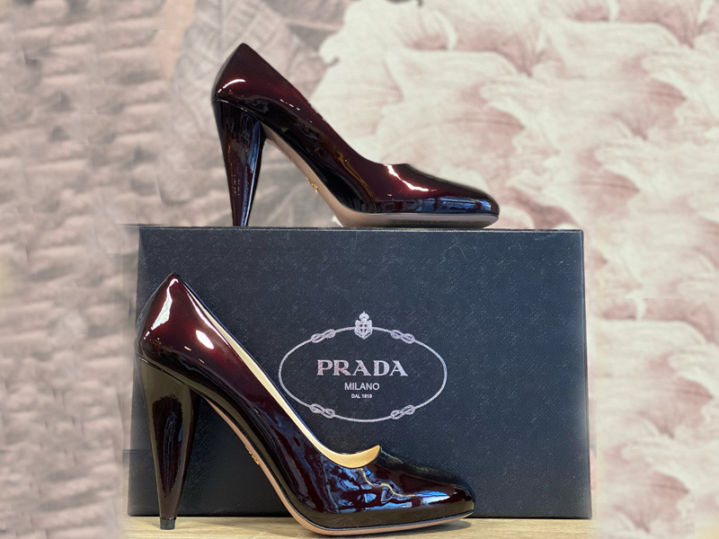 Schwarze lackierte High Heels von Prada, präsentiert auf einer eleganten Verpackung.