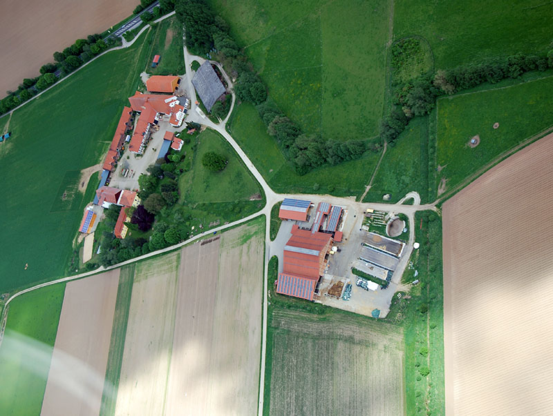 Luftaufnahme eines landwirtschaftlichen Betriebs mit Wohngebäuden, Scheunen und umliegenden Feldern.