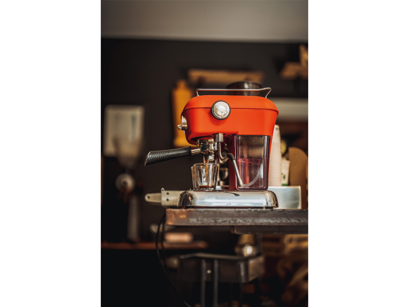 Ein roter Espresso-Maschine auf einem Tisch, bereit zur Zubereitung von Kaffee.