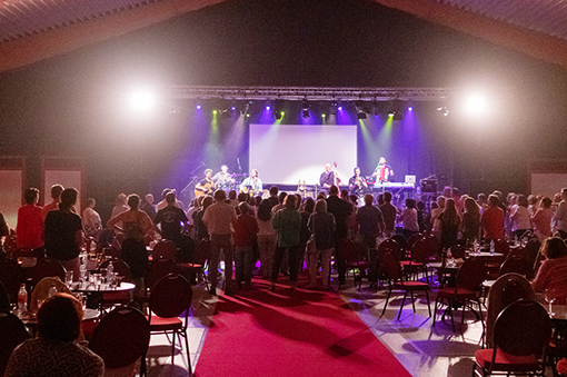 Live-Konzert mit Band auf der Bühne, Publikum mit Blick auf den Auftritt, rote Teppichfläche, beleuchteter Raum.