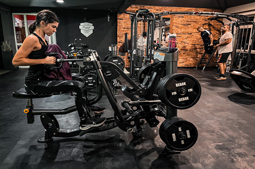 Frau trainiert an einem Fitnessgerät im modernen Fitnessstudio, im Hintergrund weitere Personen beim Training.