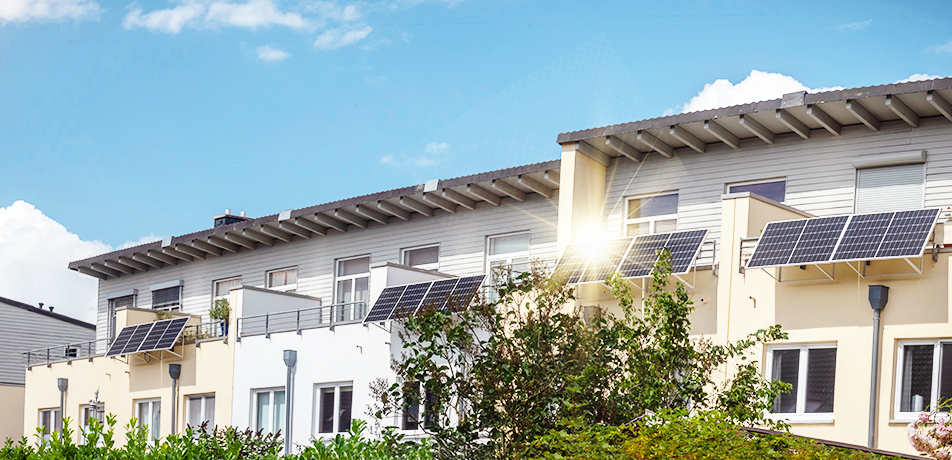 Moderne Wohnhäuser mit Solarpanelen auf den Dächern, umgeben von Grün, unter einem blauen Himmel.