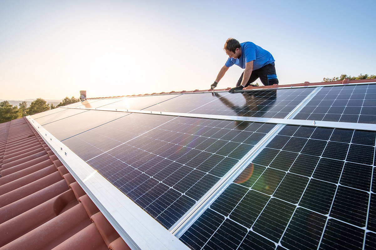 Handwerker installiert Solarpanel auf einem Dach bei Sonnenaufgang, umweltfreundliche Energiegewinnung.